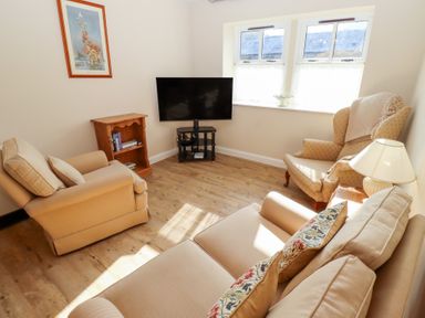 A living room with beige sofas armchair wooden floor TV and bookshelf at Catkin Cottage Akeld near Wooler