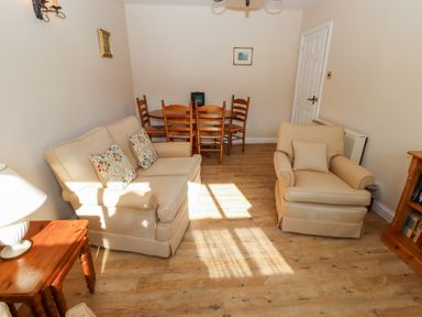 A sitting room with beige sofa and armchair wooden dining table with chairs wooden side tables and bookshelf at Catkin Cottage Akeld near Wooler