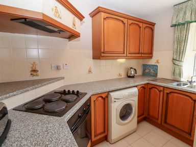 A kitchen with wooden cabinets a washing machine electric stovetop oven kettle and a window with curtains at Catkin Cottage Akeld near Wooler