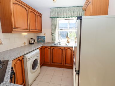 A kitchen with wooden cabinets washing machine countertop and window at Catkin Cottage in Akeld near Wooler