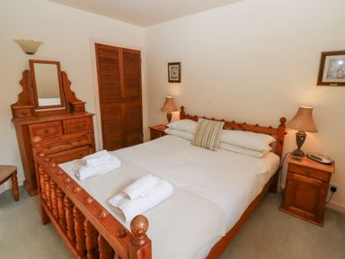 A bedroom with a wooden bed frame a dresser two bedside tables and lamps at Catkin Cottage Akeld near Wooler