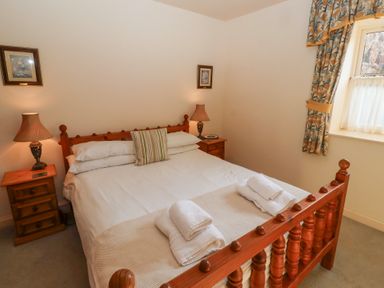 A bedroom with a wooden bed and bedside tables with lamps at Catkin Cottage in Akeld near Wooler