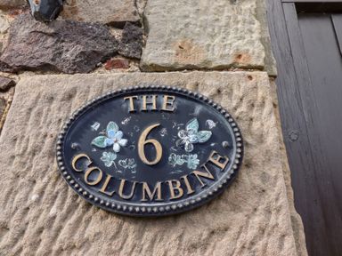 A house number plaque showing the number 6 and the name The Columbine on a stone wall at The Columbine in Akeld near Wooler