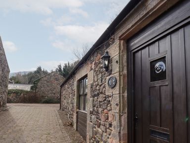 Stone buildings with a cobblestone path between them and a dark wooden door at The Columbine in Akeld near Wooler