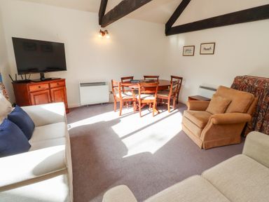 A living room with two beige sofas a brown armchair a wooden dining table with six chairs a wooden cabinet with a television and exposed ceiling beams at The Columbine in Akeld near Wooler