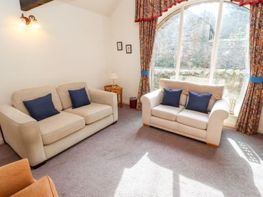 A living room with two beige sofas with blue cushions and patterned curtains by a large window at The Columbine in Akeld near Wooler