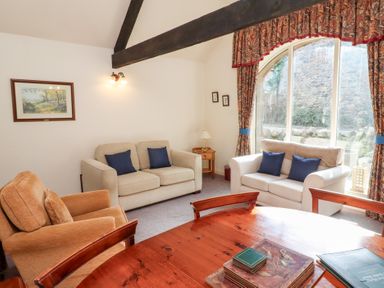 A living room with two beige sofas and an orange armchair near a large arched window at The Columbine in Akeld near Wooler