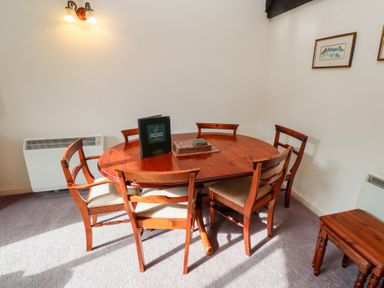 A dining area with a wooden oval table six chairs a small wooden side table and framed pictures on wall at The Columbine in Akeld near Wooler