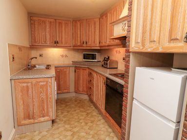A kitchen with wooden cabinets a refrigerator a microwave a toaster a sink and an oven at The Columbine in Akeld near Wooler