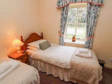 A bedroom with two single beds a nightstand with a lamp and floral curtains at The Columbine in Akeld near Wooler