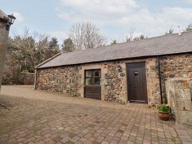 A stone cottage with a wooden door and window on a paved driveway at The Columbine in Akeld near Wooler