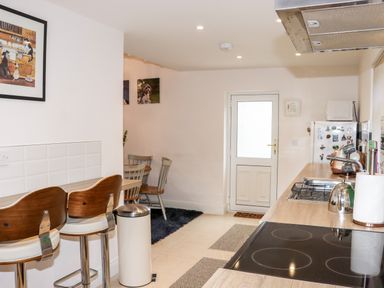 A kitchen with wooden countertops, stove, sink, bar stools, dining table, chairs, fridge, and door at Lane Cottage in Ballycullane County Wexford