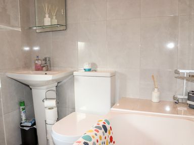 A bathroom with a white sink a toilet a bathtub a toilet paper holder and various toiletries at Lane Cottage Ballycullane County Wexford