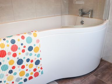 A bathroom with a white curved bathtub and a colorful polka dot towel at Lane Cottage in Ballycullane County Wexford