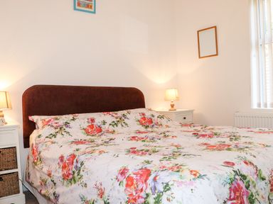A bedroom with a large bed with floral bedding two bedside tables with lamps a window and wall decorations at Lane Cottage in Ballycullane County Wexford