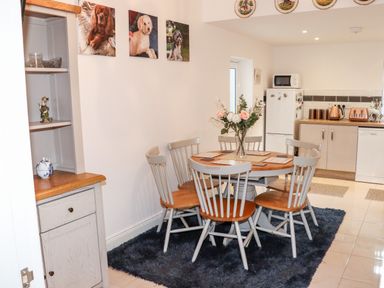 A kitchen dining area with a round wooden table surrounded by six chairs and a vase of flowers a refrigerator microwave and countertop appliances in the background at Lane Cottage Ballycullane County Wexford