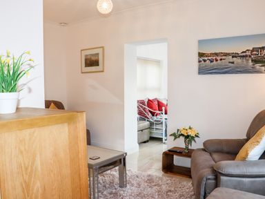 A living room with a gray armchair a wooden coffee table with flowers and a doorway leading to a room with a bed and red pillows at Lane Cottage in Ballycullane County Wexford