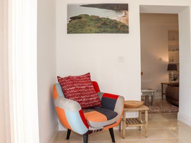 A patchwork armchair with a red cushion next to a wooden side table with a wicker tray and a wall photo of a coastal landscape at Lane Cottage in Ballycullane County Wexford