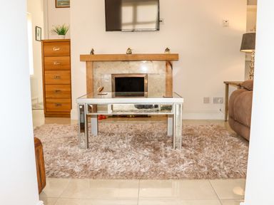 A living room with a glass coffee table on a rug in front of a fireplace with a mounted TV above at Lane Cottage in Ballycullane County Wexford