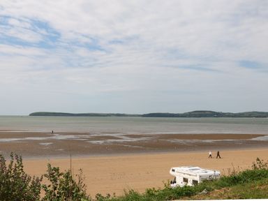 A sandy beach with three people walking and a parked camper van near the grass at Lane Cottage in Ballycullane County Wexford