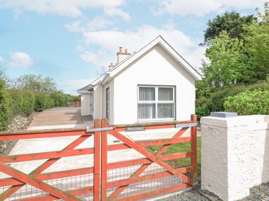 A white house with a red wooden gate and a driveway lined with hedges at Lane Cottage Ballycullane County Wexford