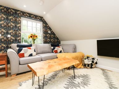 A living room with a gray sofa cushions and a wooden table with a rug on the floor and a wall-mounted TV at Robin's Nest at The Shire Inn in Killivose near Camborne