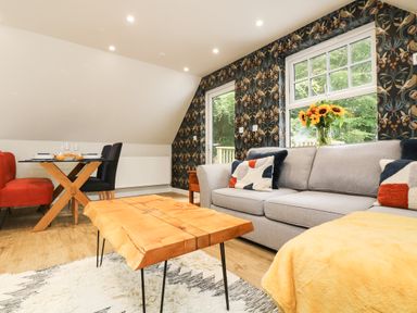 A living room with a gray sofa a wooden coffee table a dining table with chairs and a window with flowers at Robins Nest at The Shire Inn Killivose near Camborne