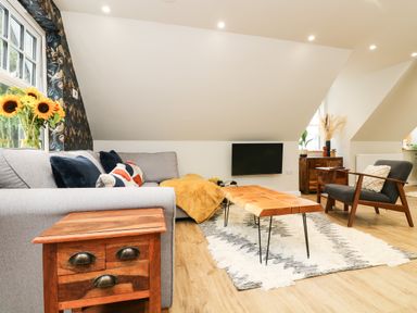 A living room with a gray sofa a wooden coffee table a wooden side table a dark gray armchair and a wall-mounted TV at Robins Nest at The Shire Inn in Killivose near Camborne