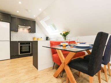 A kitchen with black cabinets white backsplash and a glass dining table with black chairs and an orange bench at Robins Nest at The Shire Inn in Killivose near Camborne