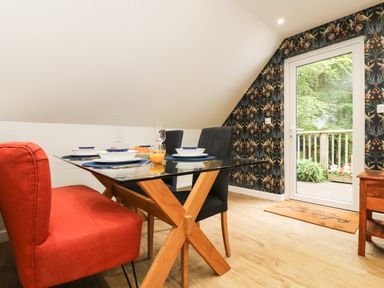 A dining area with a glass table set with plates and glasses near a door opening to a wooden deck at Robins Nest at The Shire Inn in Killivose near Camborne