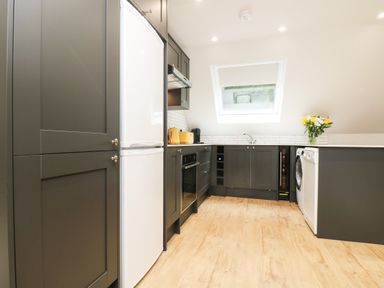 A kitchen with dark cabinets a white refrigerator an oven a washing machine a dishwasher wooden floor and a window at Robins Nest at The Shire Inn in Killivose near Camborne