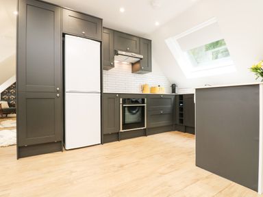 A kitchen with dark cabinets a white refrigerator an oven and a window at Robins Nest at The Shire Inn Killivose near Camborne
