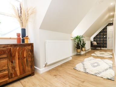 A hallway with wooden floor rugs plants a wooden cabinet and an armchair at Robins Nest at The Shire Inn Killivose near Camborne