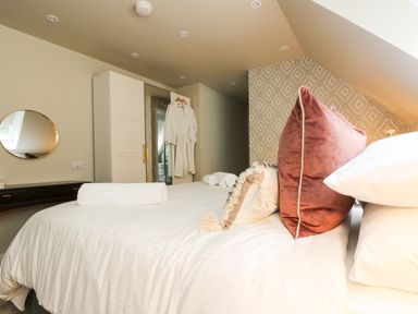 A bedroom with a bed of white linens and pillows robes hanging on a wardrobe at Robins Nest at The Shire Inn Killivose near Camborne