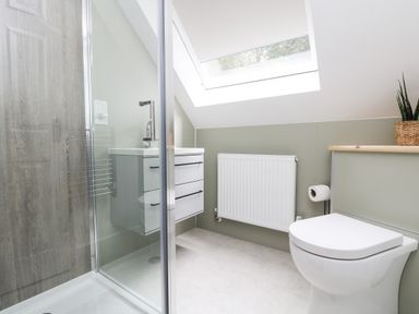 A bathroom with a shower enclosure a white toilet a white sink with drawers a radiator and a skylight window at Robins Nest at The Shire Inn in Killivose near Camborne
