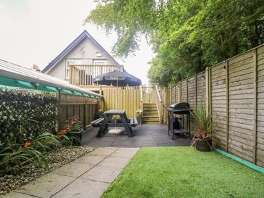 A backyard with a picnic table and umbrella a barbecue grill stone pathway and artificial grass at Robins Nest at The Shire Inn in Killivose near Camborne