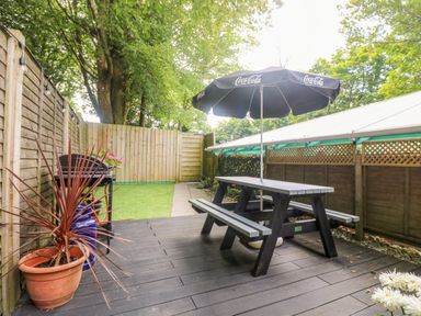 A fenced outdoor patio with a picnic table and umbrella a barbecue grill and potted plants at Robins Nest at The Shire Inn in Killivose near Camborne