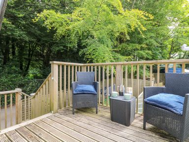 An outdoor wooden deck with two wicker chairs with blue cushions and a small table with coffee cups at Robins Nest at The Shire Inn in Killivose near Camborne
