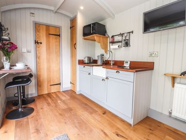 A kitchen with wooden floor blue cabinets a TV on the wall and a small dining area at The Moorhen Retreat in Nantmawr near Trefonen