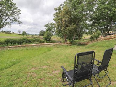 Two black outdoor chairs on grass facing trees and fields at The Moorhen Retreat in Nantmawr near Trefonen