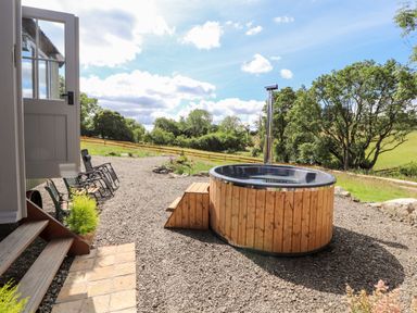 An outdoor area with a wooden hot tub gravel ground and garden chairs at The Moorhen Retreat in Nantmawr near Trefonen