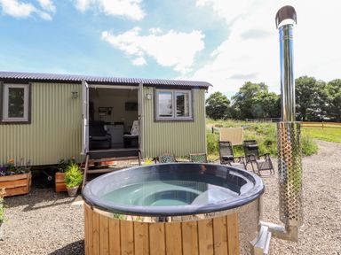 An outdoor hot tub and chairs in front of a small corrugated metal building with windows and double doors at The Moorhen Retreat in Nantmawr near Trefonen