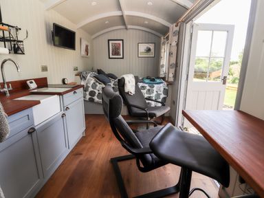 A small room with kitchenette, two chairs, a bed, and an open door showing outside at The Moorhen Retreat in Nantmawr near Trefonen