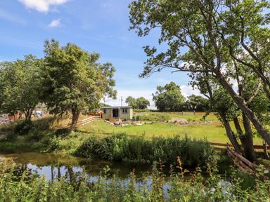 A small building with chairs outside near trees and a pond at The Moorhen Retreat in Nantmawr near Trefonen