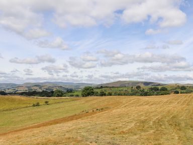 A rural landscape with fields trees and distant hills under a partly cloudy sky at The Moorhen Retreat in Nantmawr near Trefonen