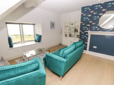 A living room with teal sofas a glass coffee table and patterned wallpaper at 21 The Rest in Porthcawl