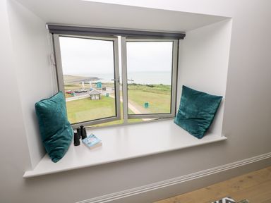 A window seat with two blue cushions a book and binoculars overlooking grassy land and the sea at 21 The Rest in Porthcawl