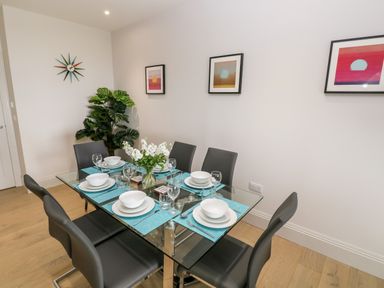 A dining room with a glass table set for six with plates glasses and a vase of flowers on a wooden floor at 21 The Rest in Porthcawl