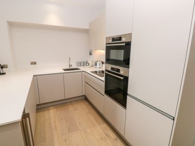 A kitchen with white cabinets wooden floor double ovens a sink and small appliances at 21 The Rest in Porthcawl