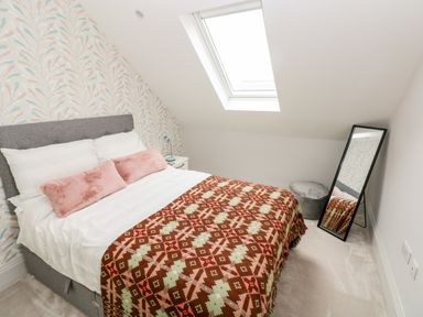 A bedroom with a bed a bedside table a lamp a standing mirror and a skylight at 21 The Rest in Porthcawl